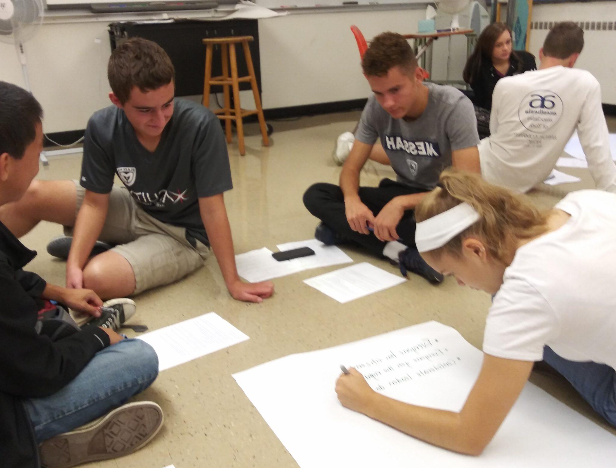 Students collaborating on a class project, drawing on paper on the floor